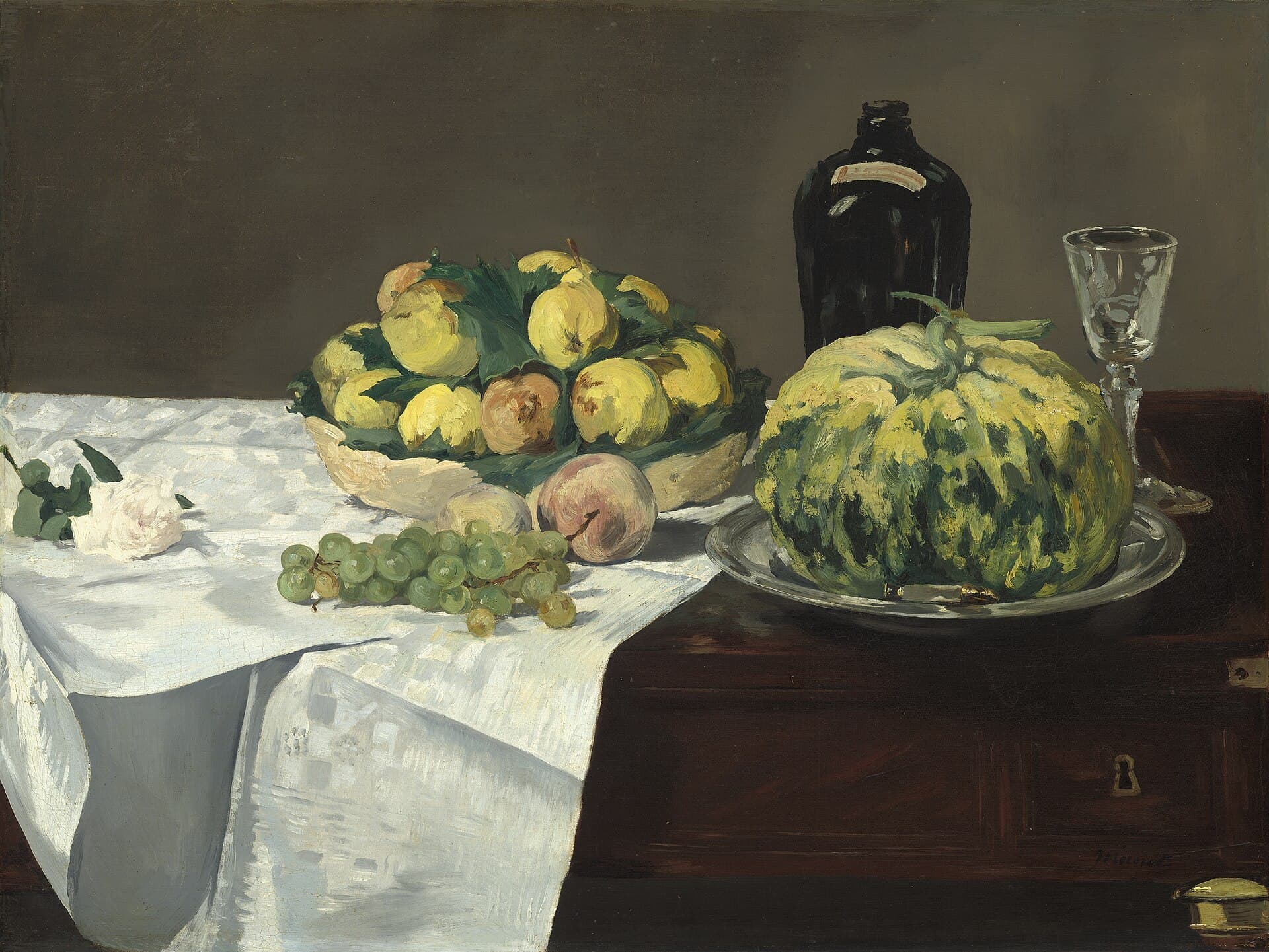 A halved green melon, white grapes, and peaches arranged on a cloth-draped stone ledge.