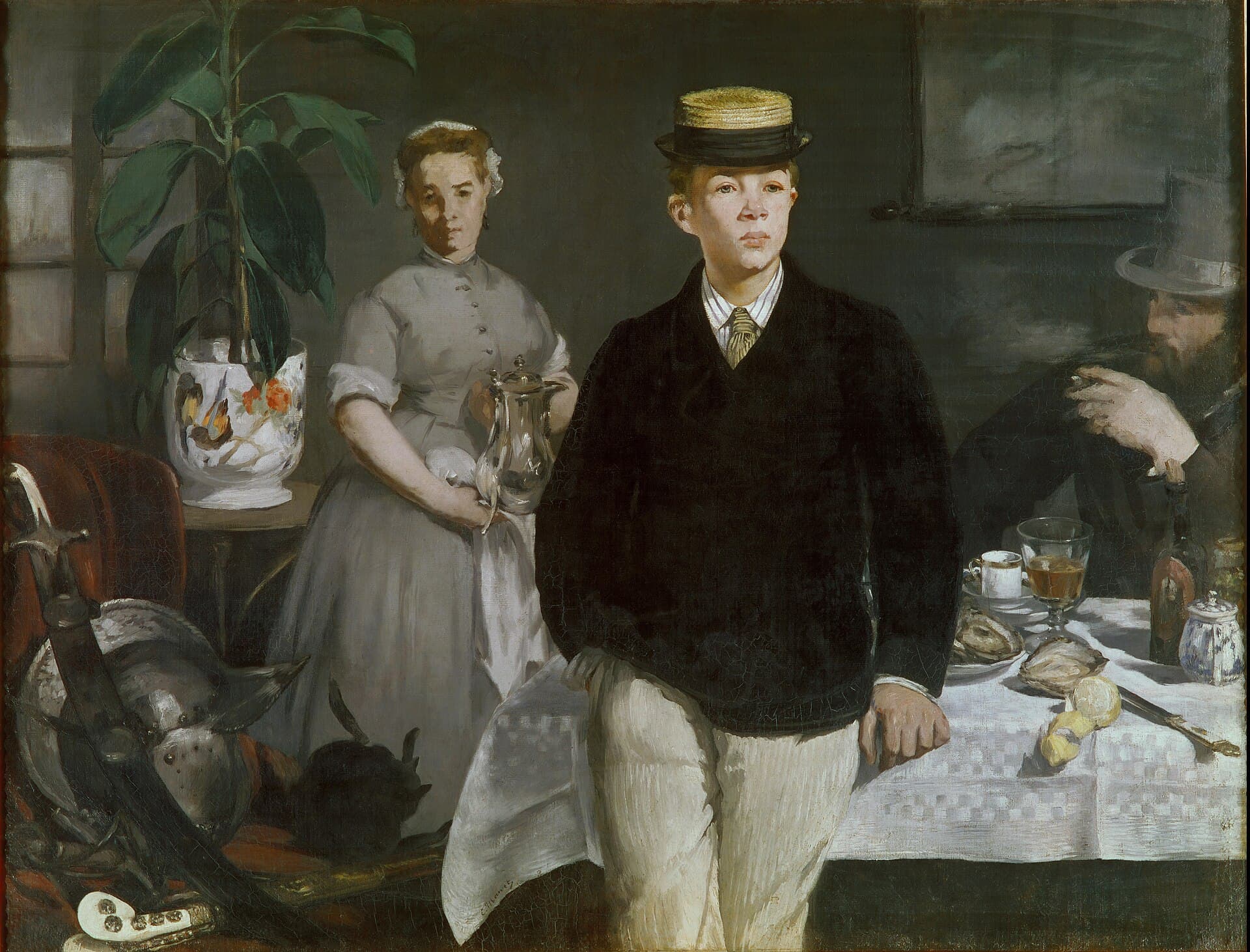 A young man in a straw boater leans against a table laid for lunch, a maid and older man visible behind him.
