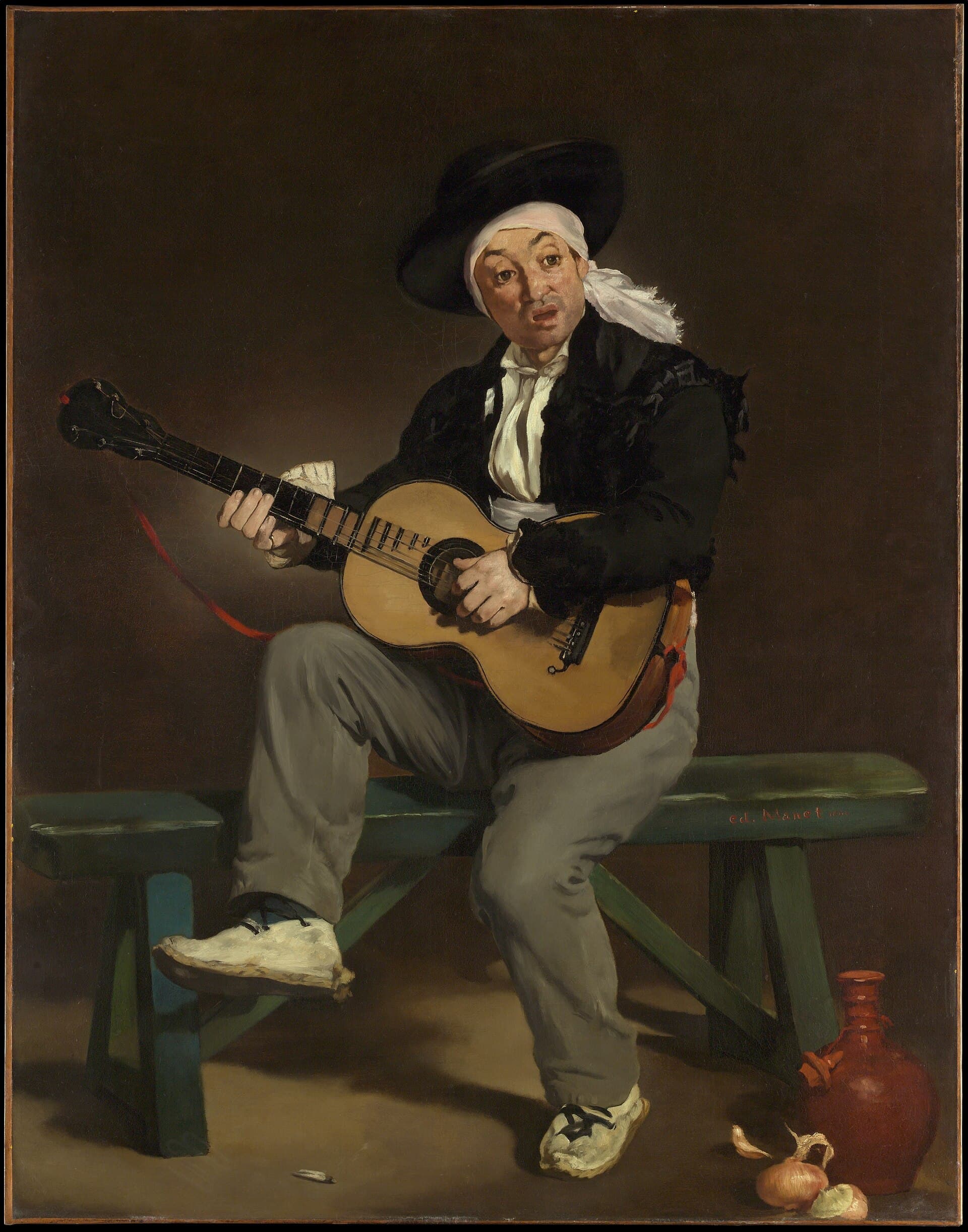 A man in Andalusian costume sits on a bench playing a guitar, a jug and onions at his feet.